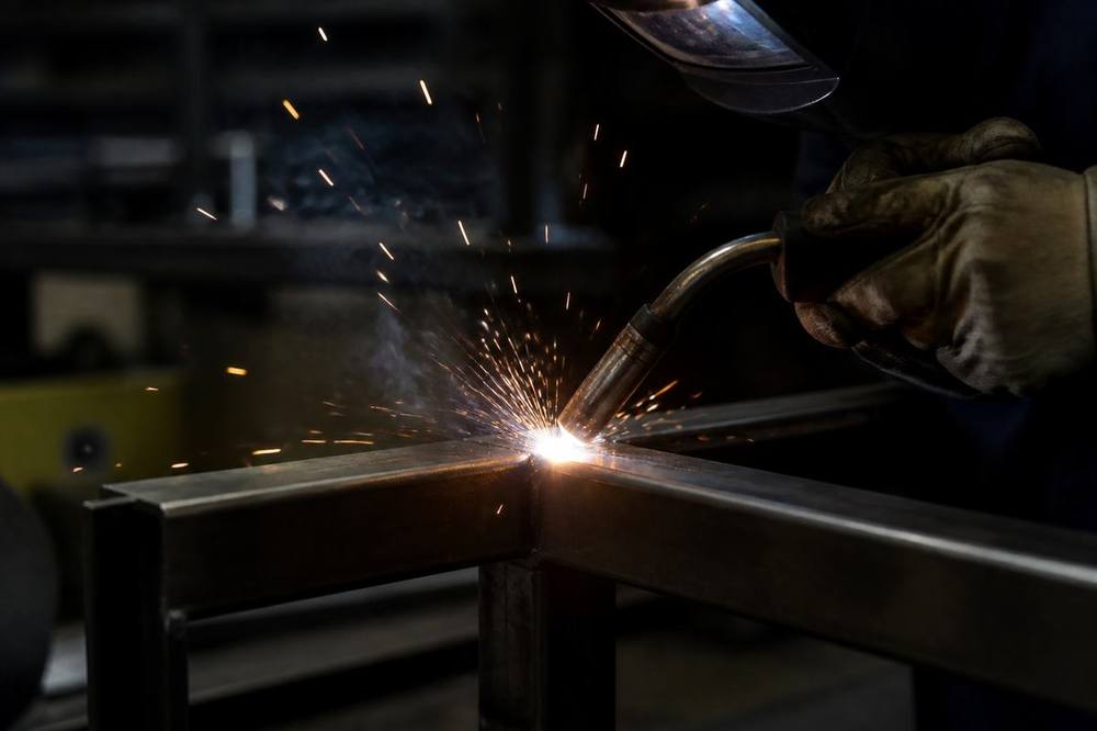 Welder joining steel with bright sparks in a dark shop